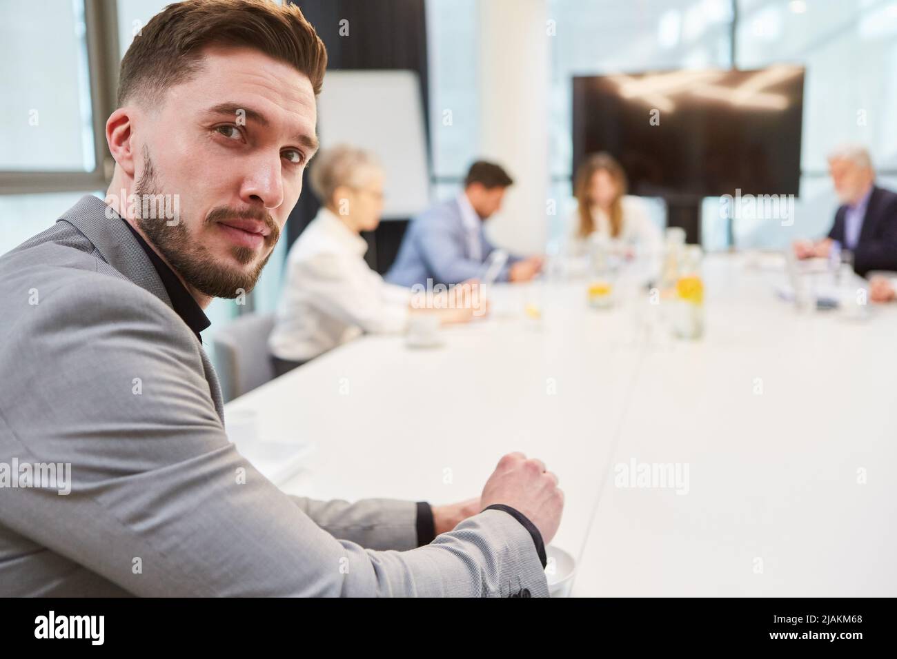 Junger Geschäftsmann als Gründerin am Konferenztisch mit einem Team im Hintergrund Stockfoto