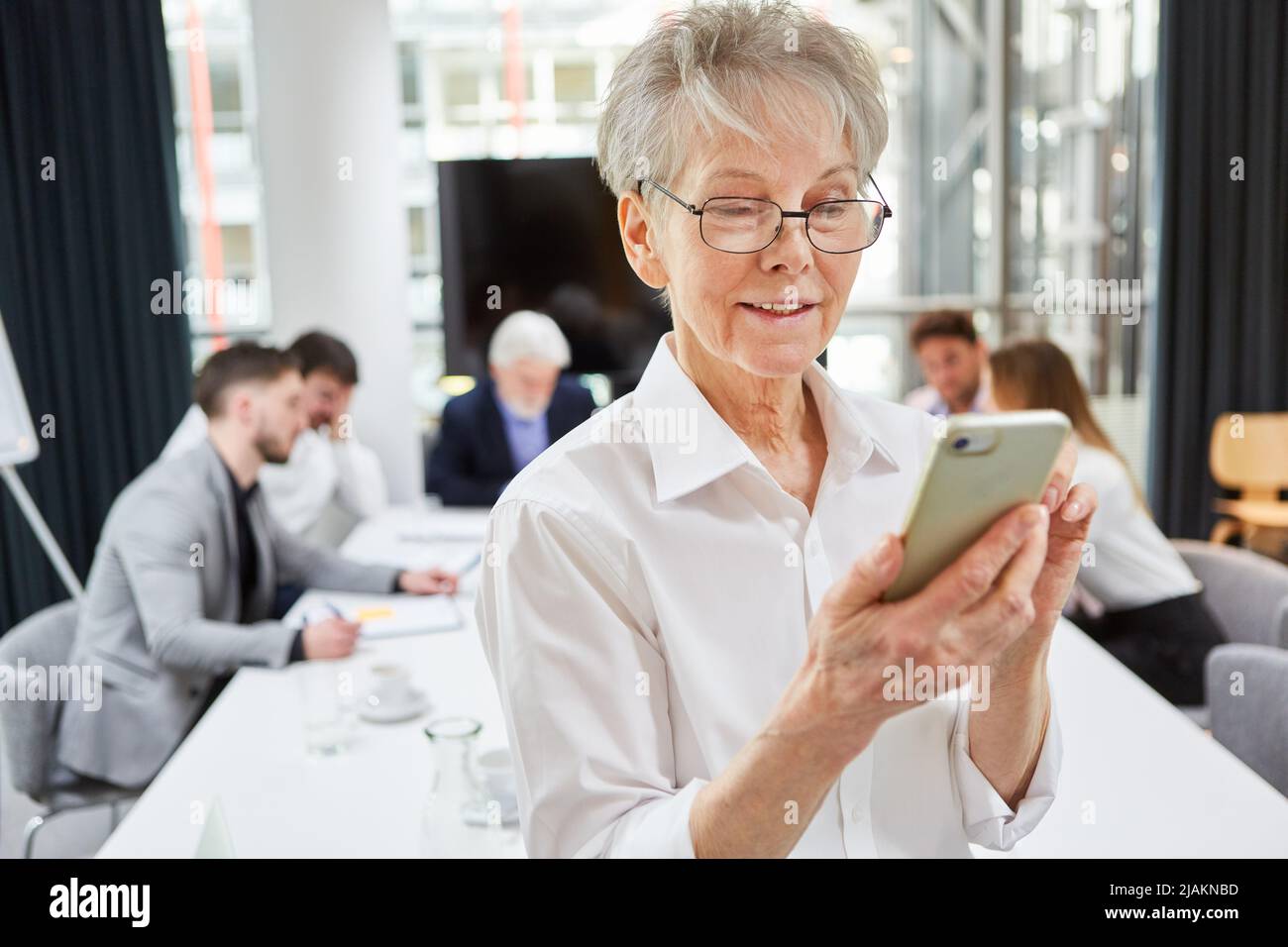 Geschäftsfrau, die während der Besprechung SMS mit Nachrichten oder Webfeeding-Nachrichten auf dem Smartphone liest Stockfoto