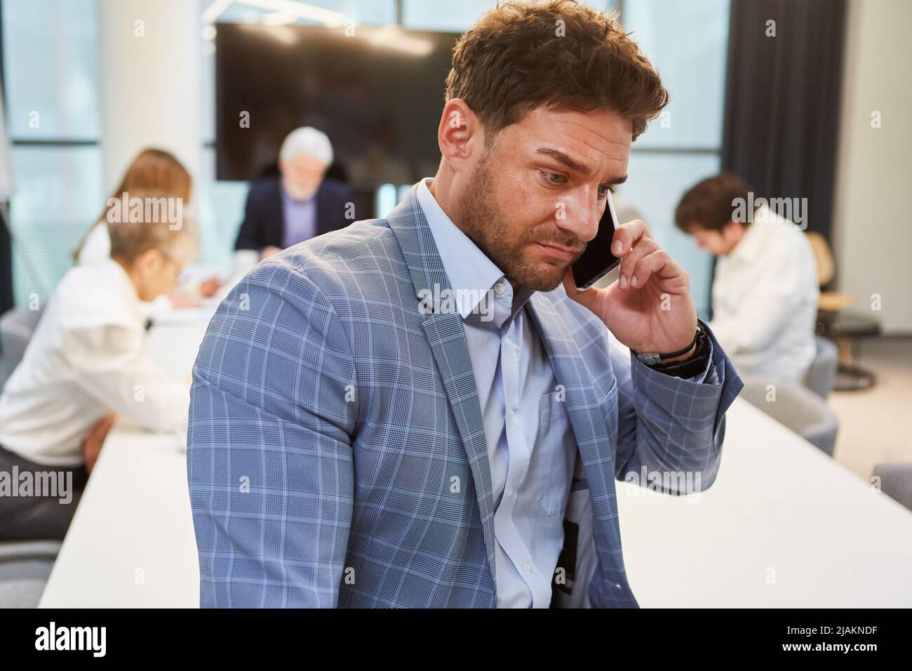 Ein Geschäftsmann spricht im Konferenzraum mit dem Smartphone und dem Team im Hintergrund Stockfoto