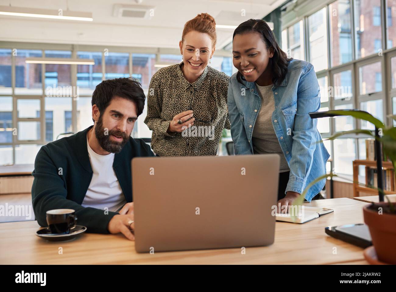 Eine bunte Gruppe lächelnder junger Geschäftsleute, die an einem Laptop arbeiten Stockfoto