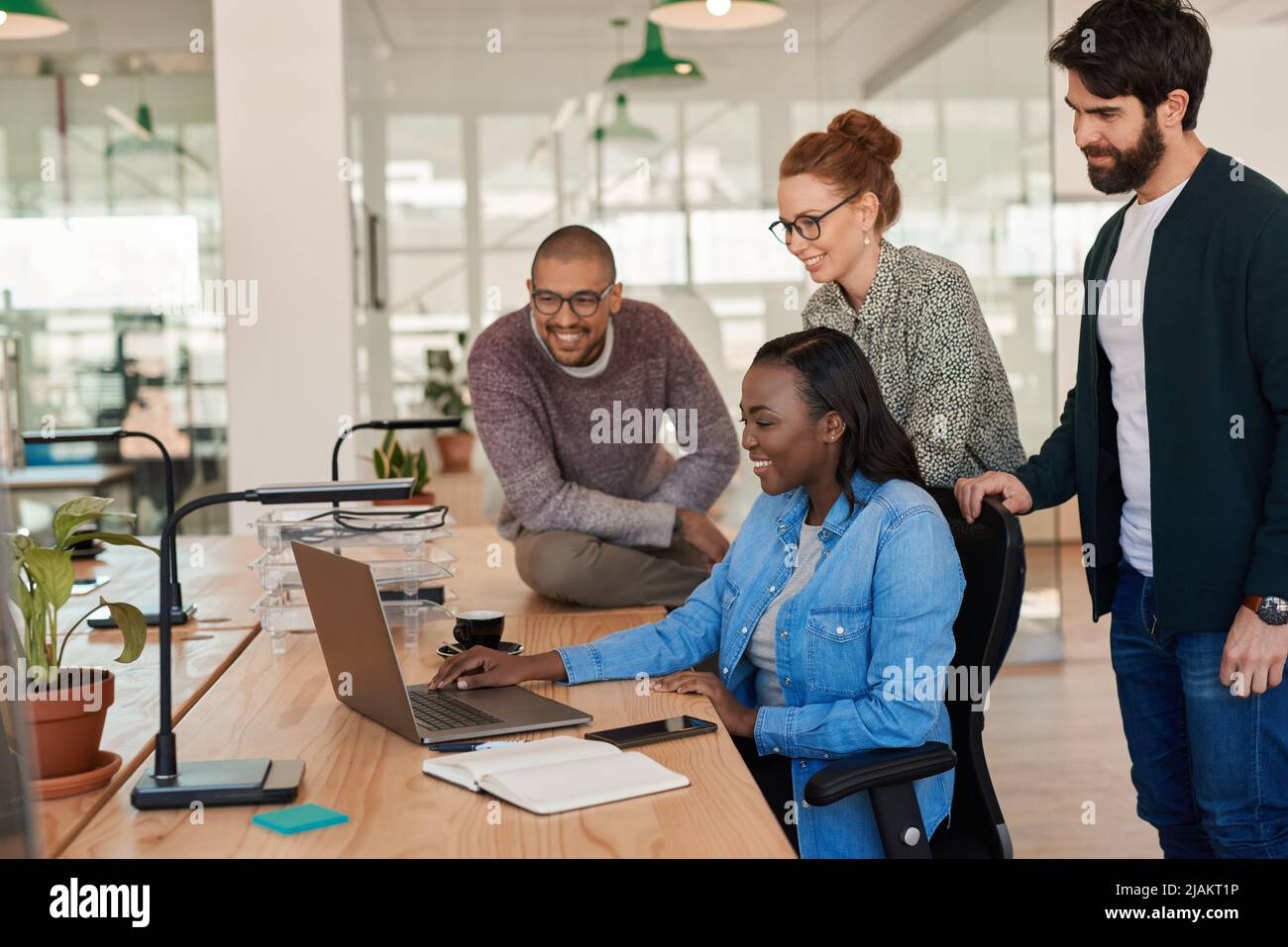 Eine Gruppe lächelnder Geschäftsleute, die um einen Laptop herum zusammenarbeiten Stockfoto