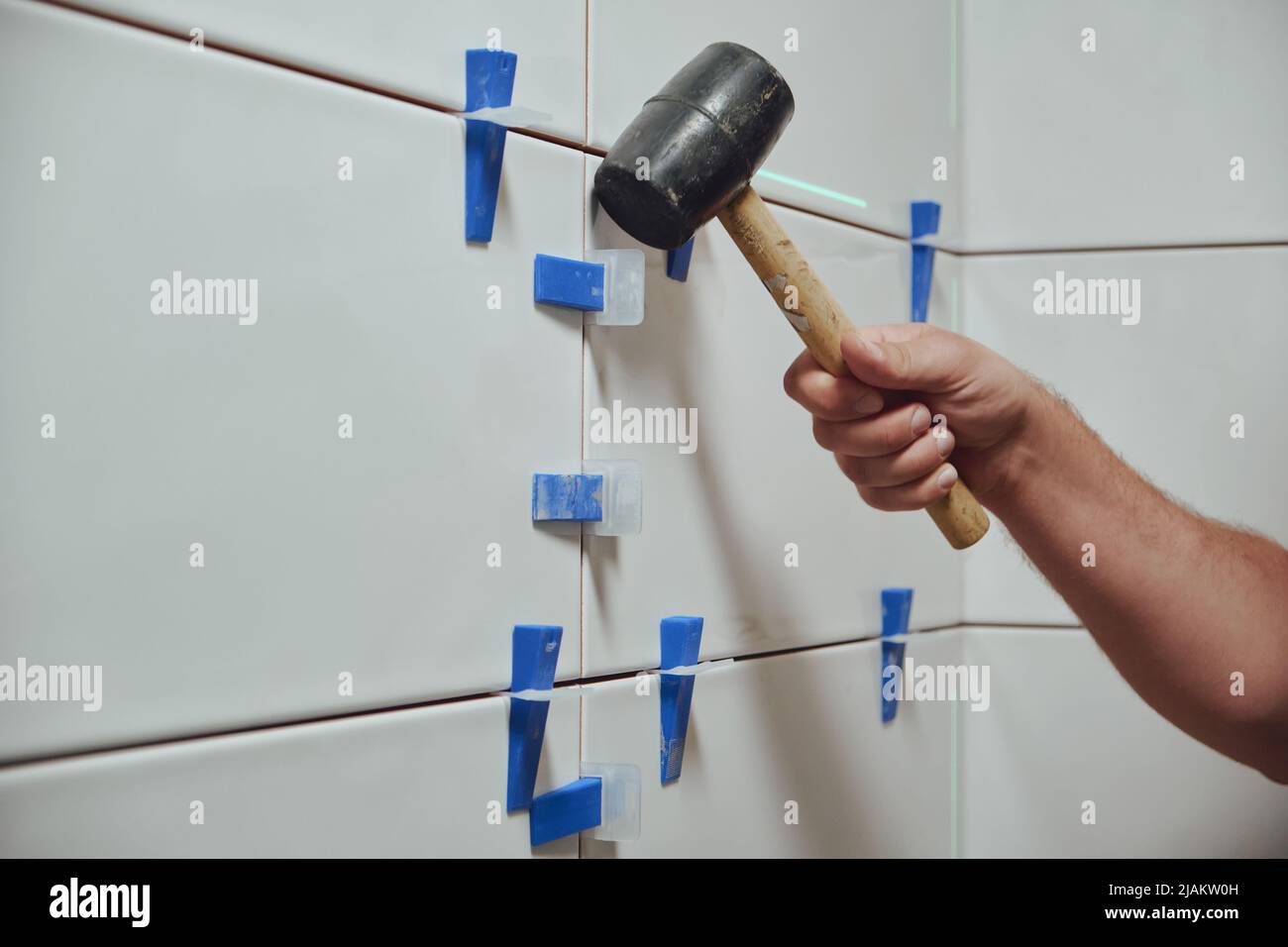 Fliesenleger klopft die Keile des Keramikfliesen-Nivelliersystems von der Wand im Badezimmer Stockfoto