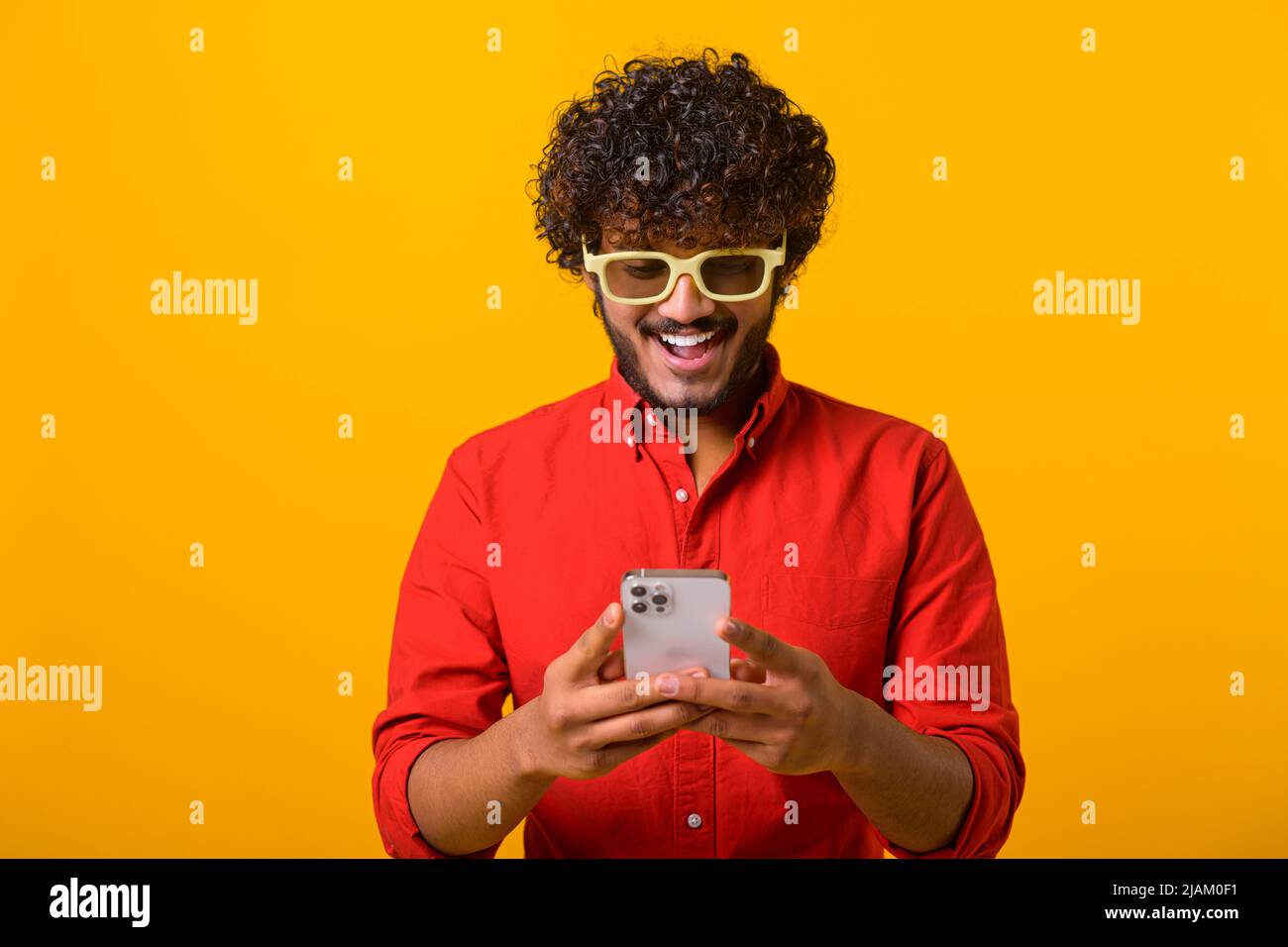 Porträt von fröhlichen Brünette Mann mit Bart mit Handy und lächeln, lesen gute Nachricht, genießen mobile Anwendung. Innenaufnahme des Studios isoliert auf orangefarbenem Hintergrund Stockfoto