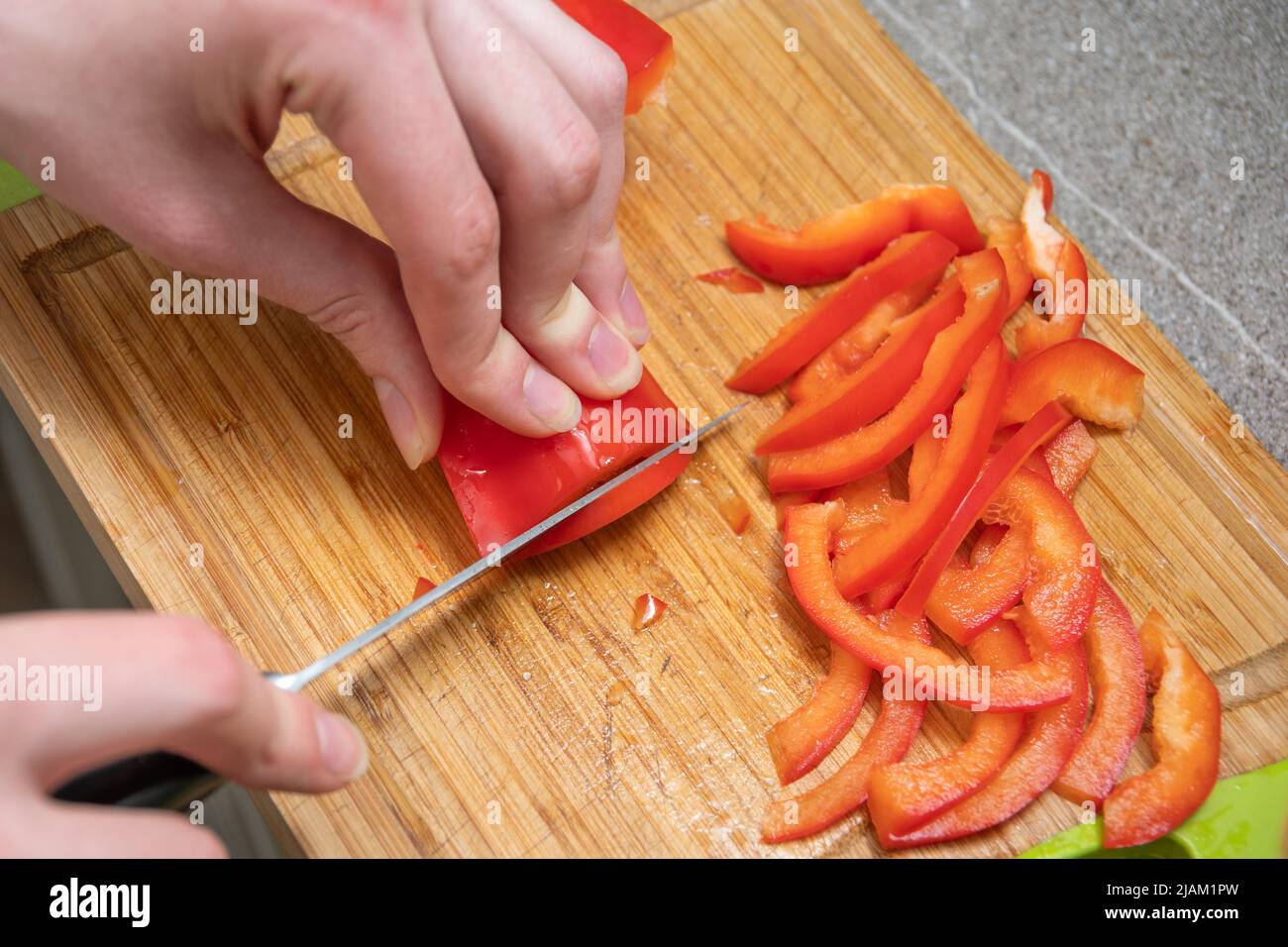 Weibliche Hände schneiden rote saftige rohe Paprika auf einem Brett, Nahaufnahme. Das Konzept des Kochens von hausgemachten Speisen. Salat in der Küche zubereiten. Diät Essen conce Stockfoto