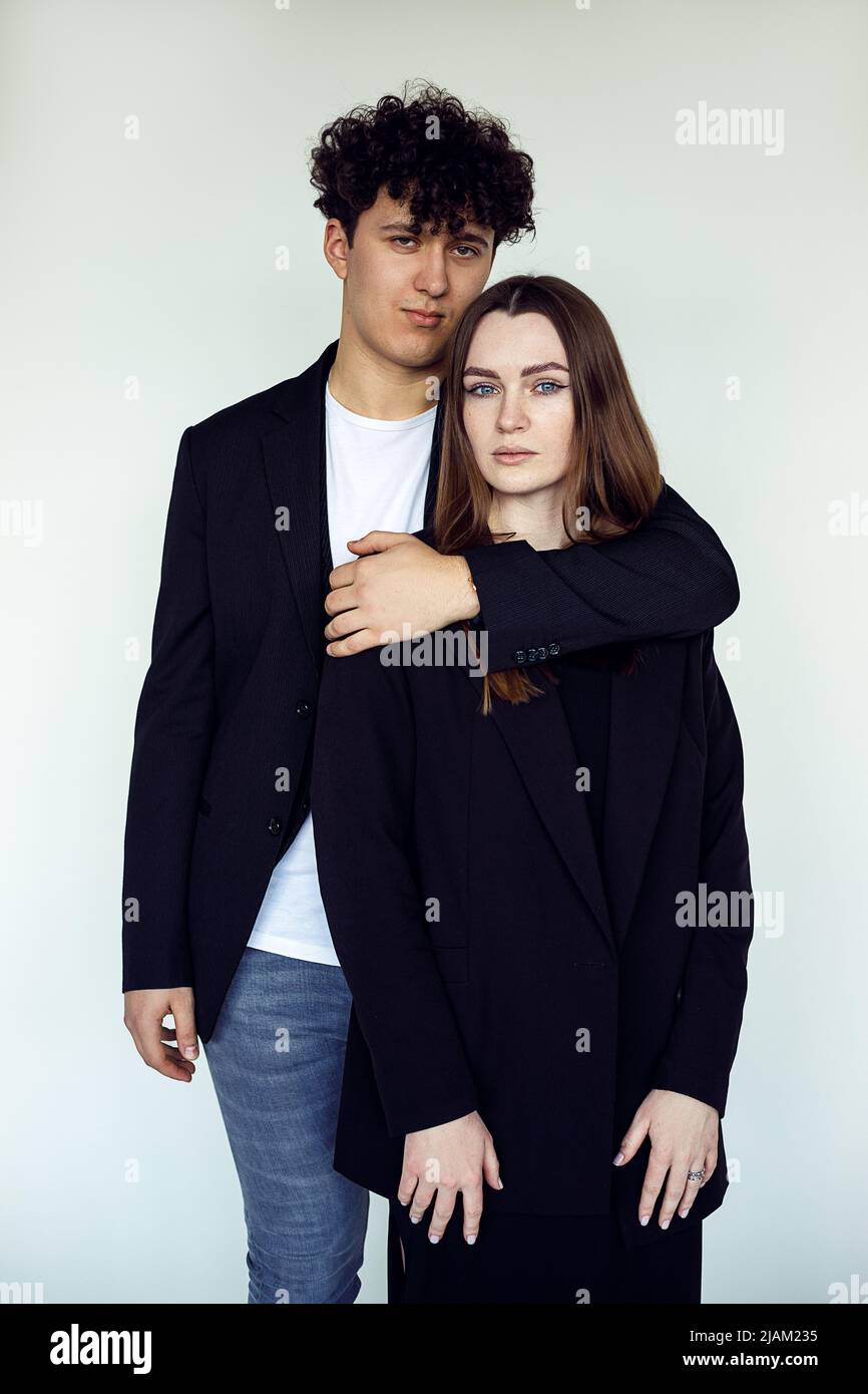 Vertikales Porträt von jungen attraktiven braunhaarigen Mann und Frau in schwarzer Kleidung stehen zusammen, umarmt. Weiße Ansicht Stockfoto