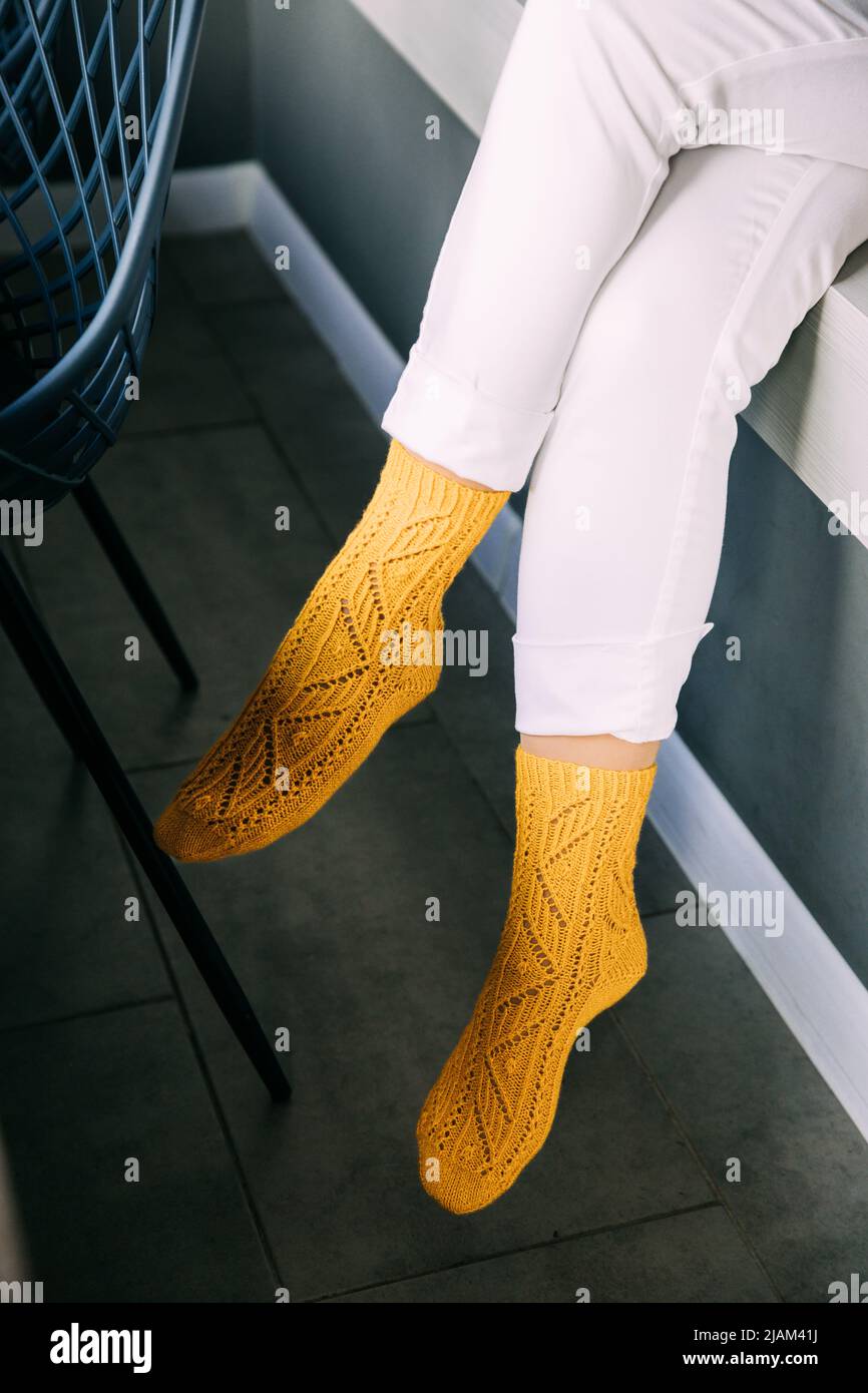 Weibliche Beine in weißen Hosen und gelben Stricksocken. Gemütliche Zeit Stockfoto