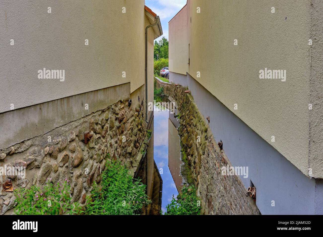 Schmale Lücke zwischen zwei Häusern, durch die ein kleiner Bach fließt; im historischen Stadtzentrum von Waren, Mecklenburg-Vorpommern, Deutschland. Stockfoto
