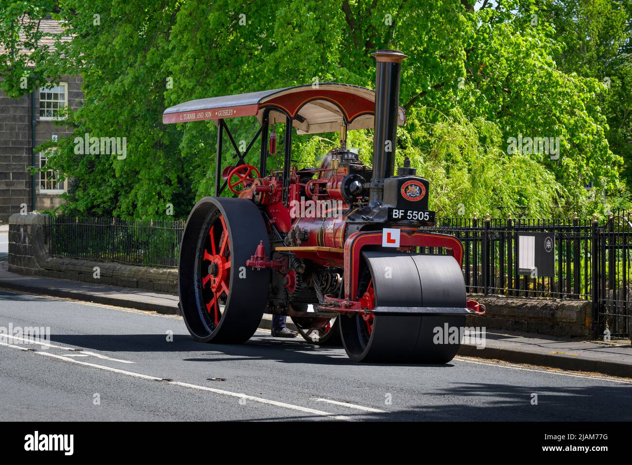 Rot-schwarzes, stationäres, schweres Dampffahrzeug, das am Straßenrand geparkt ist (L-Schild und Kennzeichen vorne) - Burley-in-Wharfedale, West Yorkshire England, Großbritannien. Stockfoto