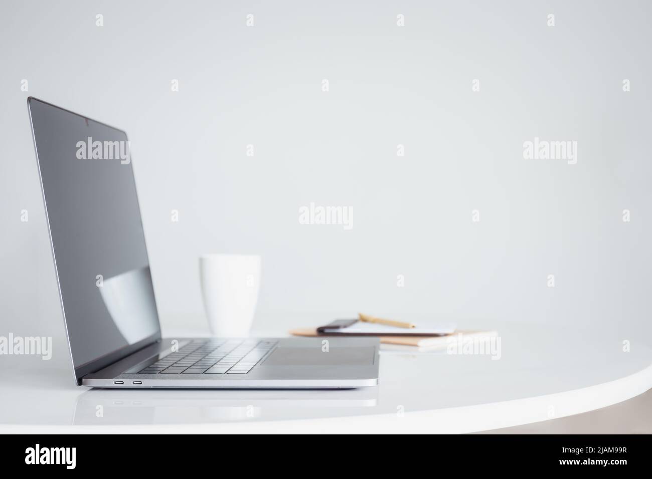 Offener Laptop-Computer mit Kaffee und Notebook auf weißem Tisch. Stockfoto