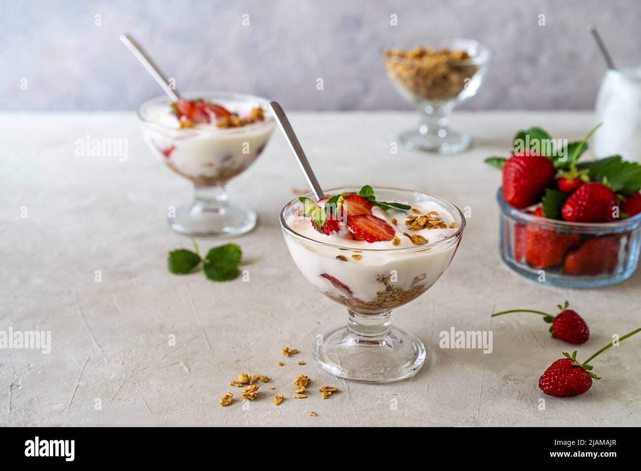 Joghurt mit Erdbeerkompott und Müsli, mit frischen Früchten in Dessertbechern auf grauem Hintergrund. Speicherplatz kopieren Stockfoto