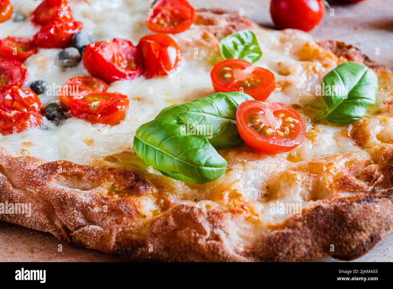 Kleine hausgemachte vegetarische Pizza mit Zusatz von Tomaten, Kapern auf einem rustikalen Holztisch Stockfoto