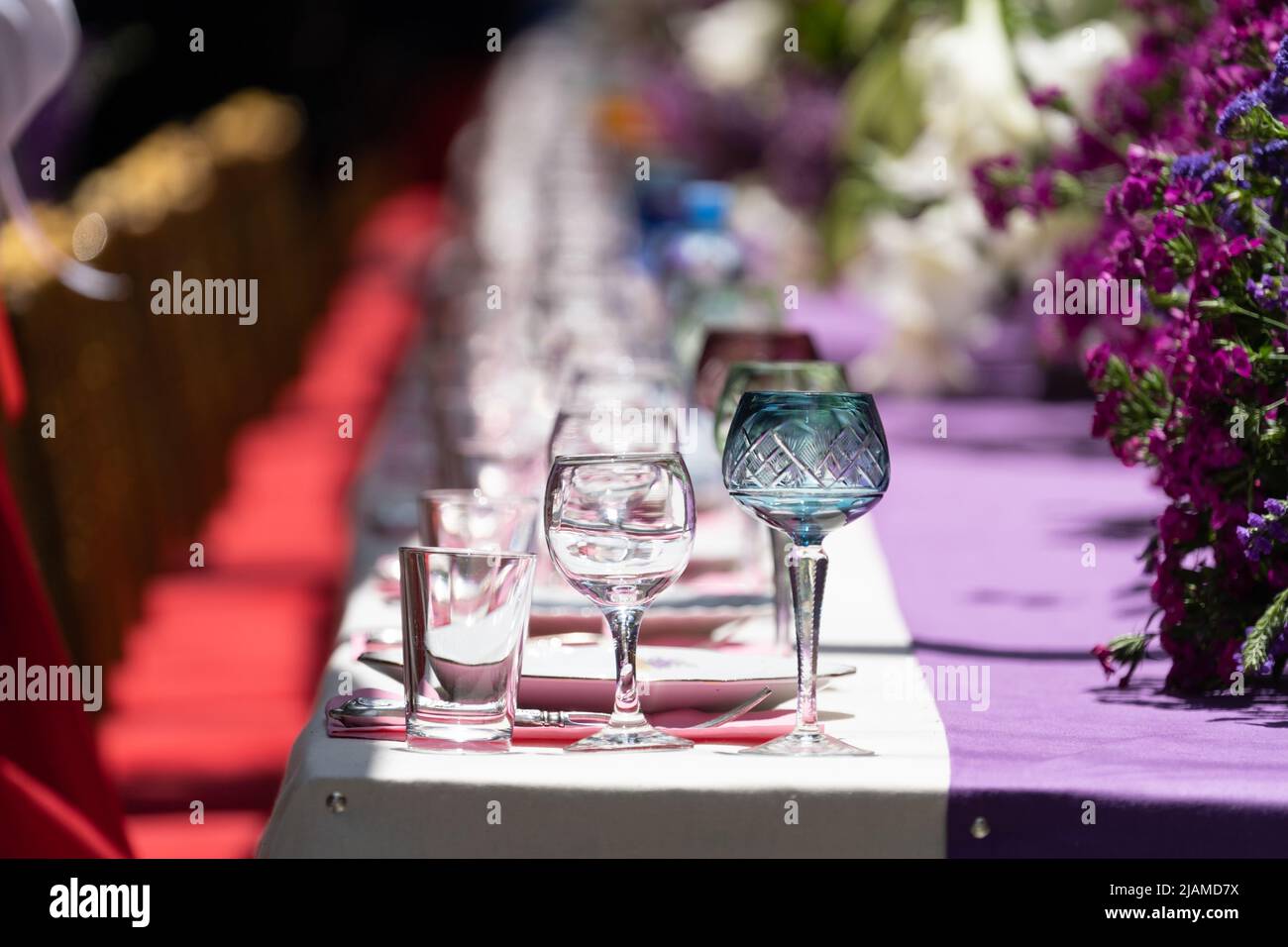 Großer Tisch mit leerem Geschirr in der Nähe von roten Stühlen für den Urlaub im Freien bei sonnigem Wetter. Weichfokus. Stockfoto