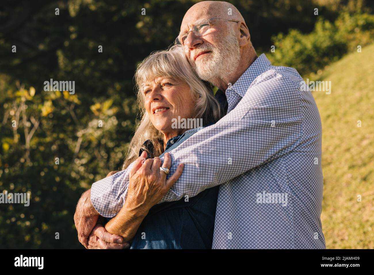Romantisches Seniorenpaar umarmt sich gegenseitig, während es in einem Park steht. Ältere Paare, die sich gegenseitig die Sonne in den Armen genießen. Reifes Paar, das Qua ausgibt Stockfoto