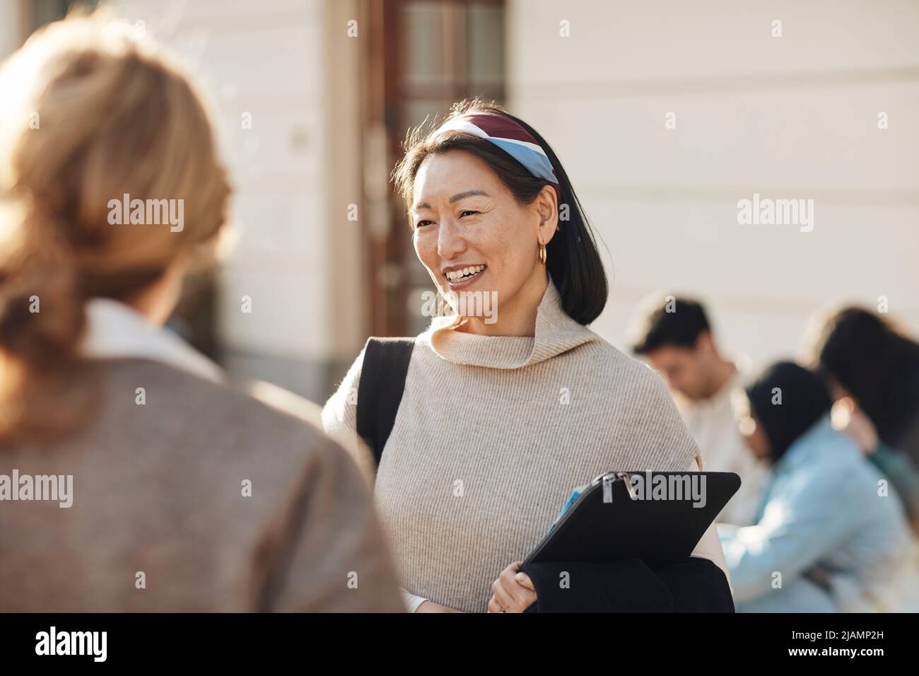 Lächelnde Lehrerin, die die Kollegin auf dem Universitätscampus anschaut Stockfoto