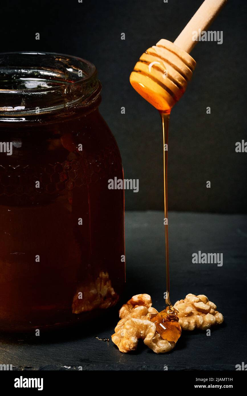 Glas mit rohem Bio-Honig und Löffel gießt Honig über eine Walnuss Stockfoto