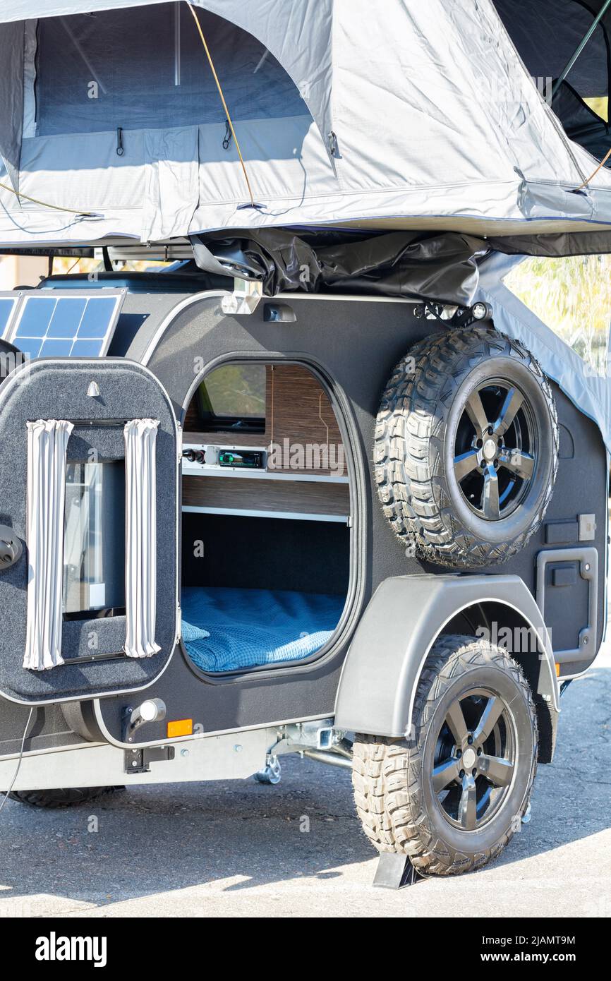 Ein kleines Wohnmobil-Haus auf einem Wohnwagen mit Solarbatterie und einem Klappzelt mit Schlafplätzen auf dem Dach für den mobilen Tourismus. Stockfoto