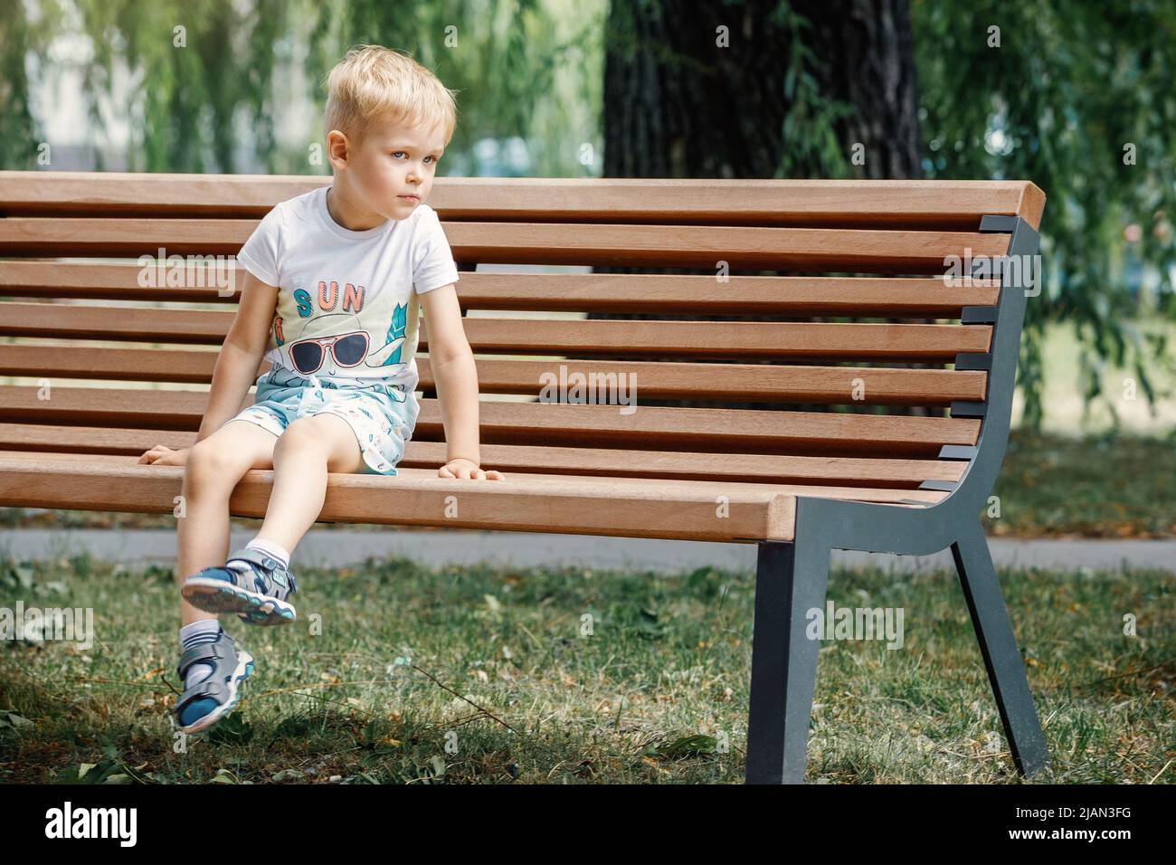 Kleiner Junge im Sommer Stadt Park sitzt auf einer Bank. Stockfoto