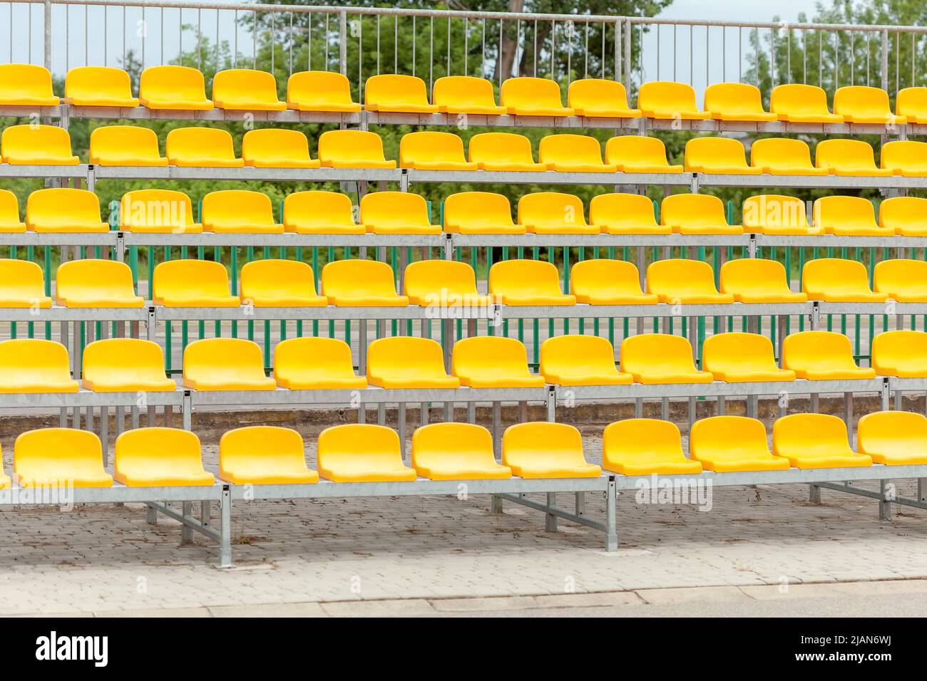 Leere Stadionstände, Stühle, Zuschauersitze in der gelben Kunststoffarena auf einem kleinen Fußballfeld, tagsüber, Pfanne, niemand. Keine Menschen, Sport ev Stockfoto