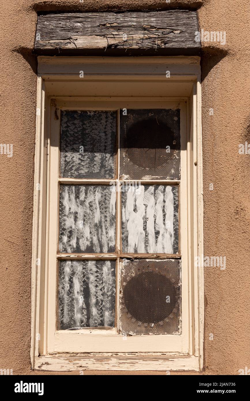 Ein Fenster mit sechs Scheiben und einem Türsturz mit abblätternder Farbe, die Scheiben des Fensters weiß gestrichen, im historischen Teil von Santa Fe, New Mexico. Stockfoto