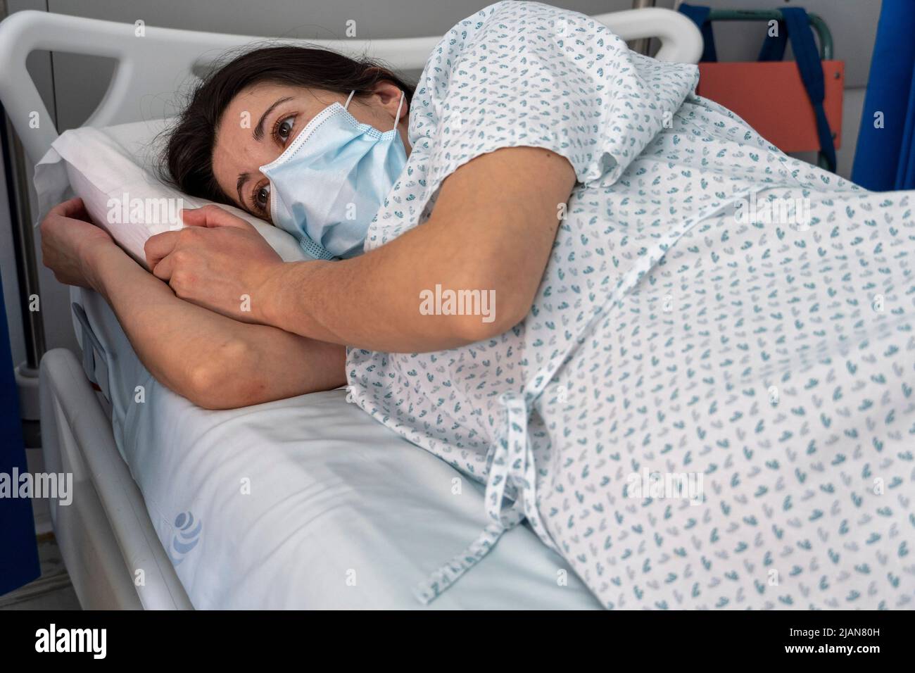 Im Krankenhaus eingewiesenen jungen Frau, die eine Gesichtsmaske trägt, während sie in einem Krankenhausbett liegt Stockfoto