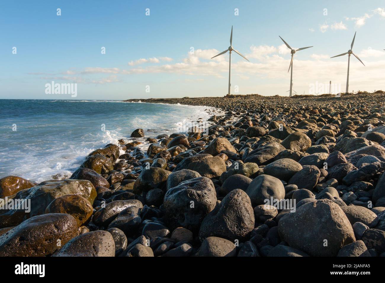 Windräder neben einem Kiesstrand in Pozo links, auf der Insel Gran Canaria bei Sonnenuntergang. Konzept für saubere Energie Stockfoto