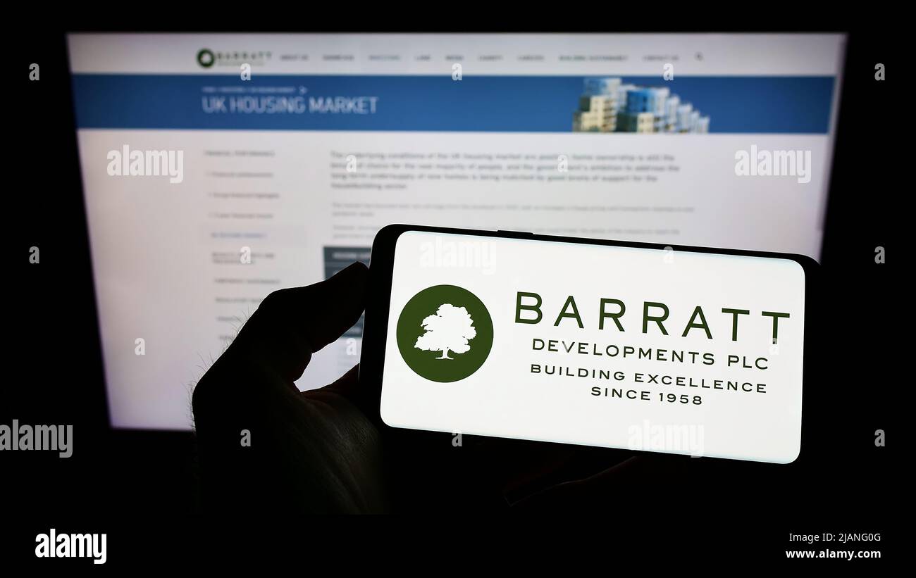 Person mit Mobiltelefon und Logo der Immobiliengesellschaft Barratt Developments plc auf dem Bildschirm vor der Geschäftswebseite. Konzentrieren Sie sich auf die Telefonanzeige. Stockfoto