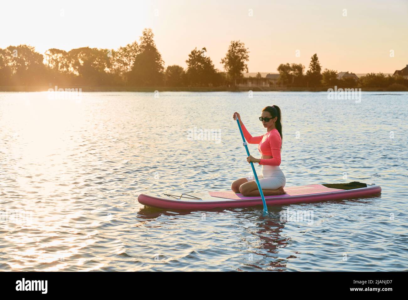 Kaukasische sportliche Frau, die am Abend auf dem See zum Training im Paddle-Boarding ist. Konzept der Menschen, aktives Hobby und gesunde Lebensweise. Stockfoto
