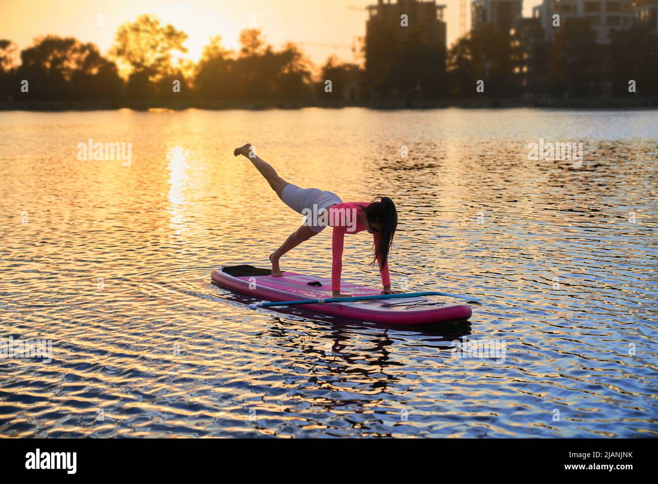Fit junge Frau Training auf Paddle Board während Sommer Sonnenuntergang über dem See. Kaukasische Frau mit braunem Haar genießen Lieblings-Aktivhobby an der frischen Luft. Stockfoto