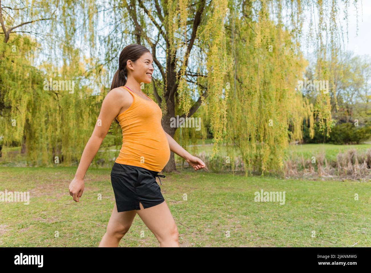 Eine Schwangerin, die im Sommer im Stadtpark spazieren geht, um ein gesundes, aktives Körpertraining zu absolvieren. Cardio-Spaziergang während der Schwangerschaft Stockfoto