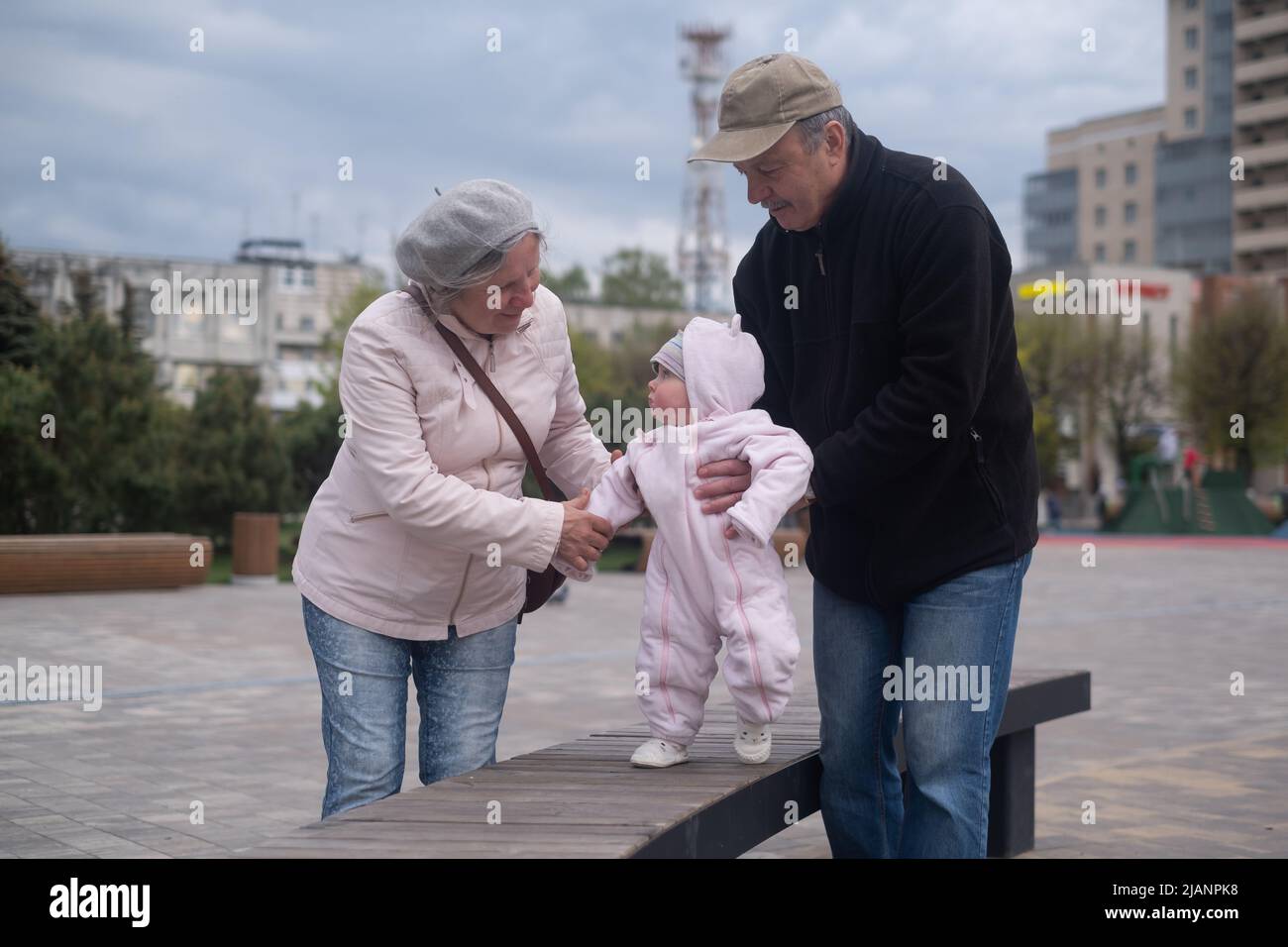 Kleines Mädchen, das mit Mann und Frau im Freien läuft. Großvater und Großmutter helfen der Enkelin beim Gehen Stockfoto