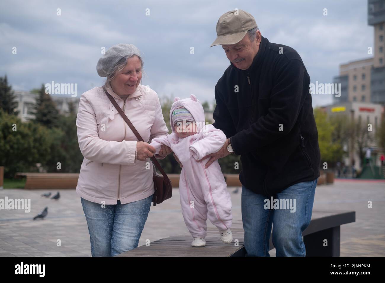 Kleines Mädchen, das mit Mann und Frau im Freien läuft. Großvater und Großmutter helfen der Enkelin beim Gehen Stockfoto