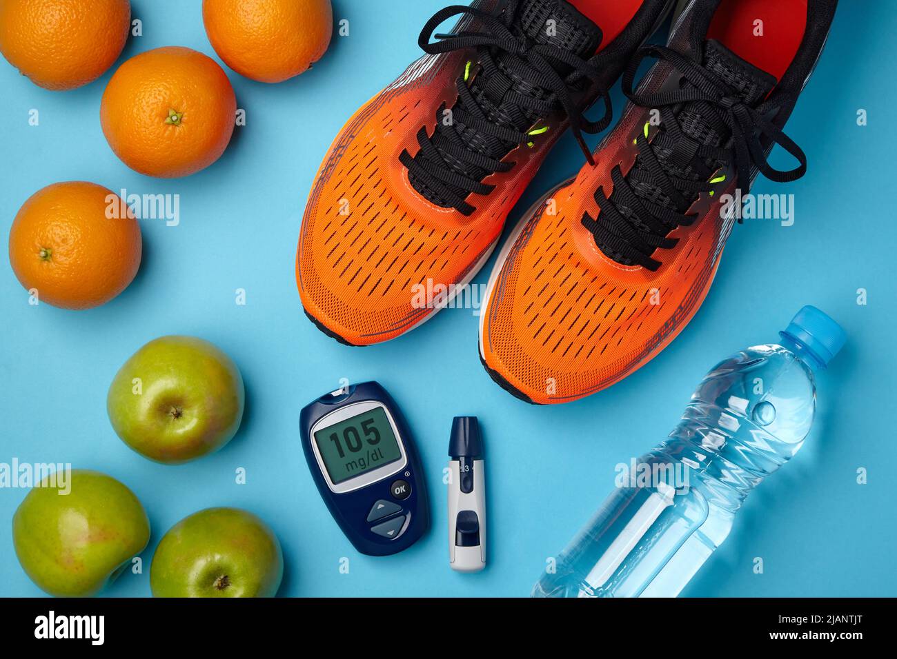 Orangefarbene Turnschuhe, Äpfel, Orangen und ein Blutzuckermessgerät auf blauem Hintergrund. Diabetes-Lebensstil. Insulinresistenz Stockfoto