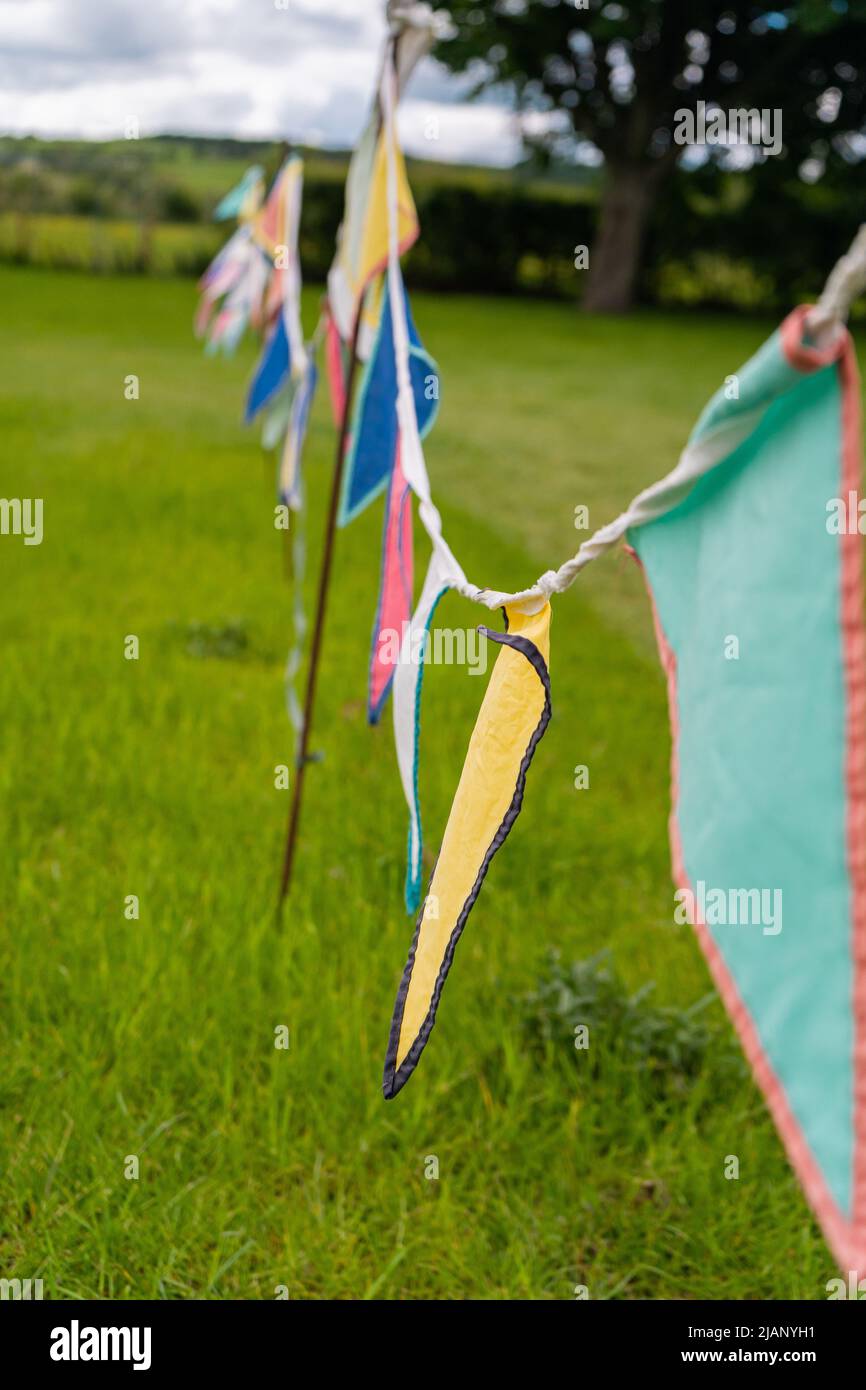 Bunte Ammer fliegen mit dem Wind auf grünem Grasfeld im Frühjahr. Triangle-Flaggen in vielen Farben streckten sich über das Feld, um ein zu markieren Stockfoto