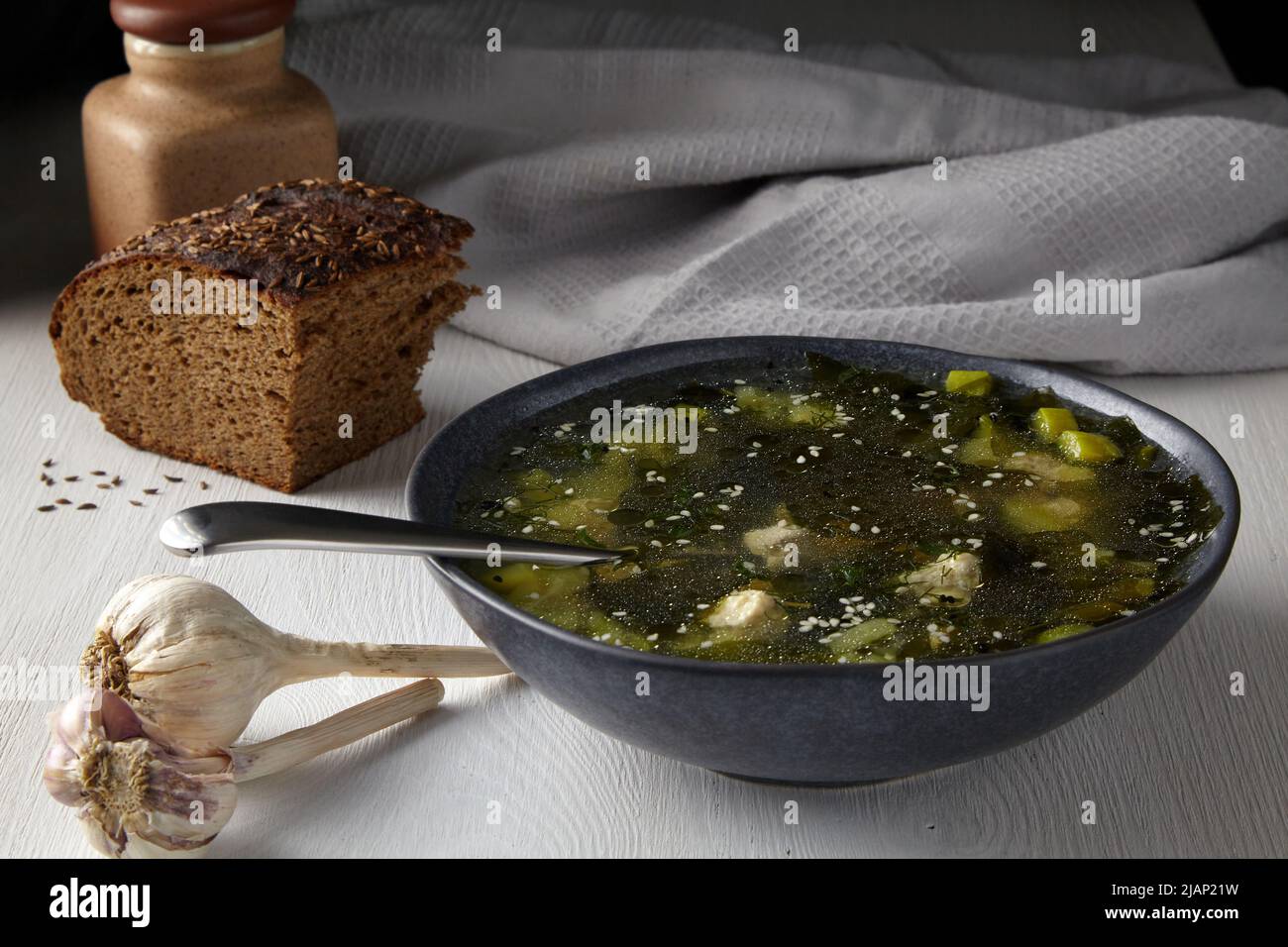 Rustikales Mittagessen im Licht vom Fenster. Zucchini-Suppe mit Fleischbällchen mit einem Stück schwarzem Brot mit Kümmel auf einem weißen Tisch gegen die BA Stockfoto