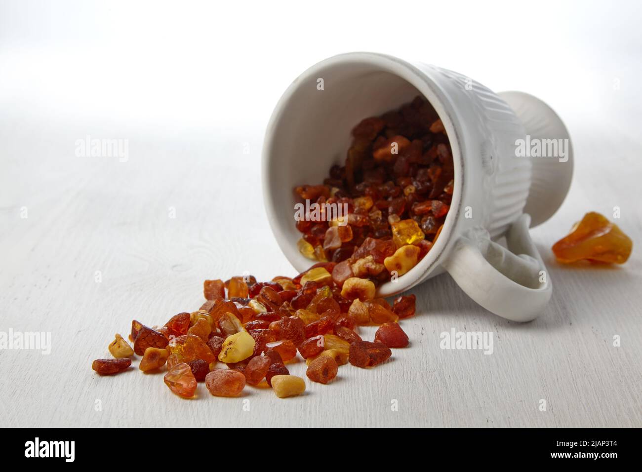 Roher Bernstein in einer Keramikschale, bestreut auf einem weißen Holztisch. Stockfoto