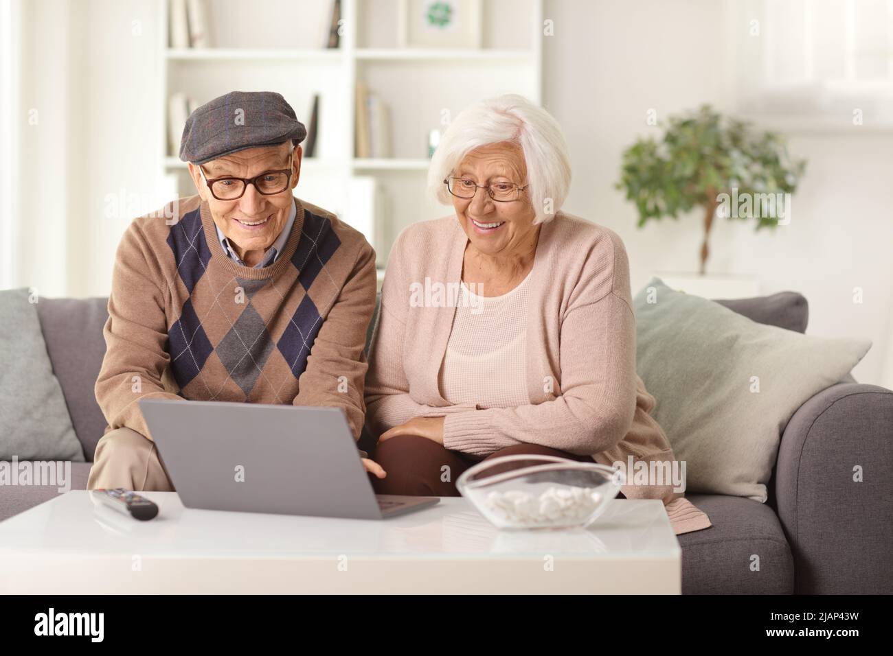 Ein älteres Paar, das zu Hause auf einem Sofa sitzt und einen Laptop anschaut Stockfoto
