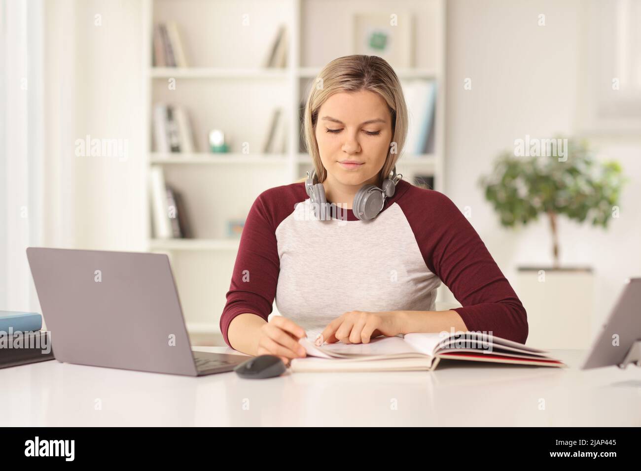 Studentin, die vor einem Laptop studiert und zu Hause ein Buch liest Stockfoto