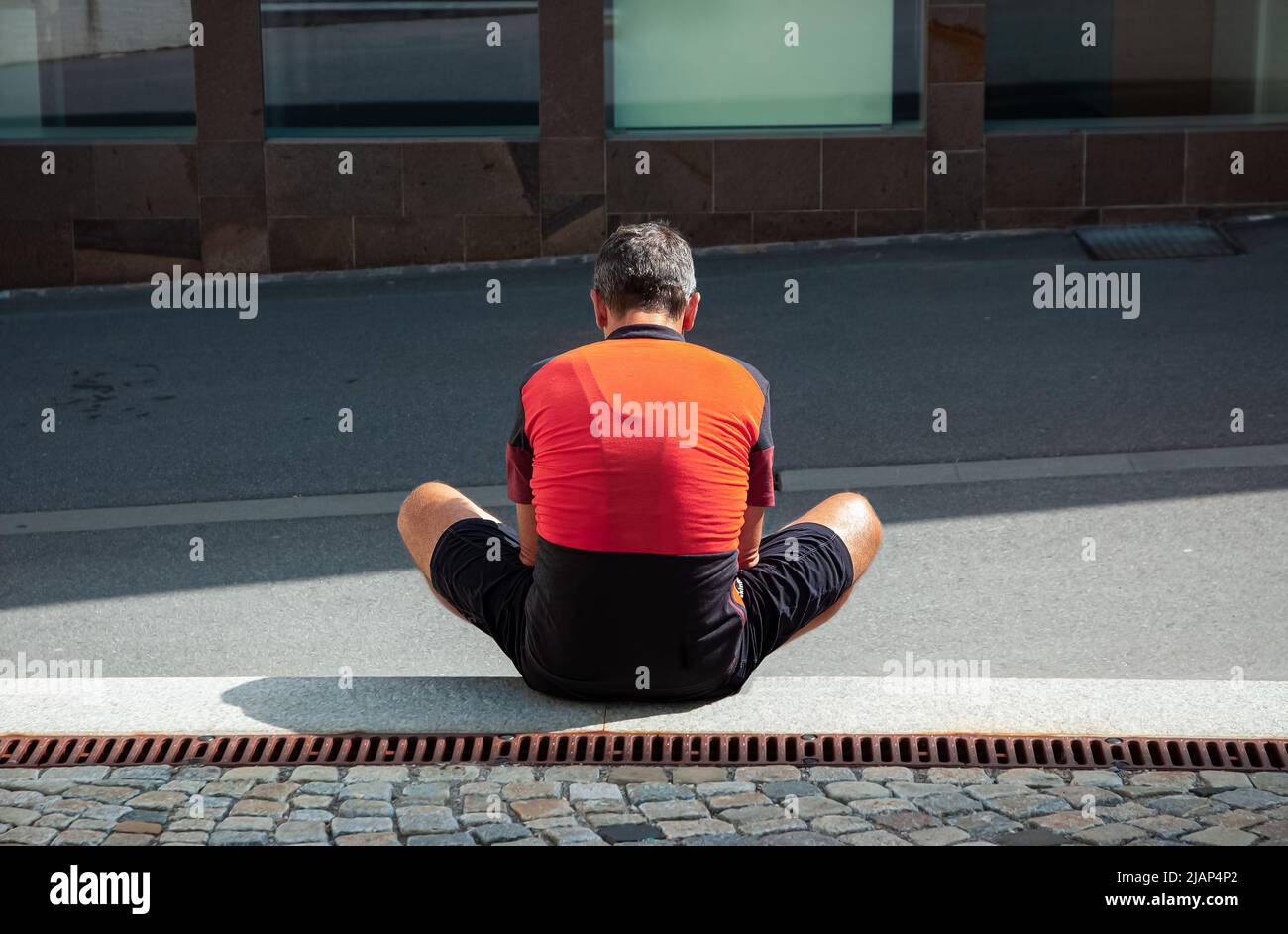 Ein einsamer Mann in einem orange-schwarzen Radtrikot sitzt an einem sonnigen Tag auf dem Boden Stockfoto