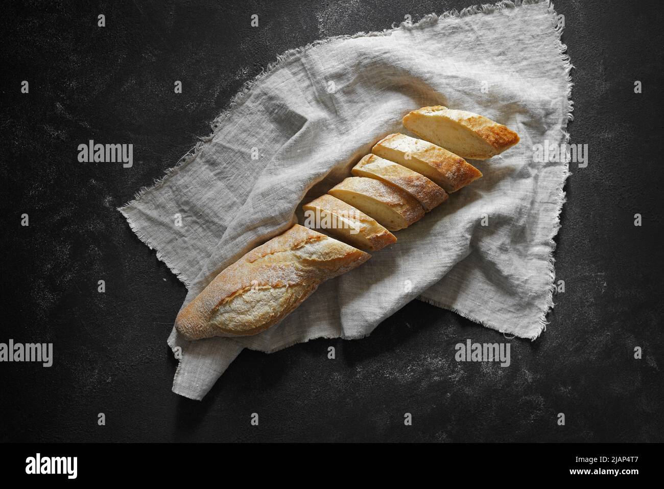 Knusprig frisch geschnittenes Baguette auf Leinenserviette auf schwarzem Tisch. Draufsicht. Stockfoto