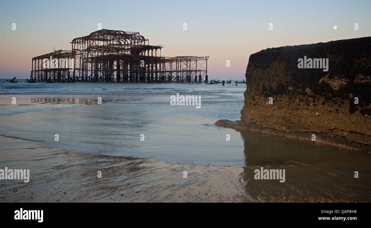 Rostreste des verfallenen West Pier bei Ebbe im Morgengrauen. Brighton & Hove, Sussex, England, Großbritannien. Vollmond. Groyne und Pool von seichtem Wasser im Vordergrund. Stockfoto