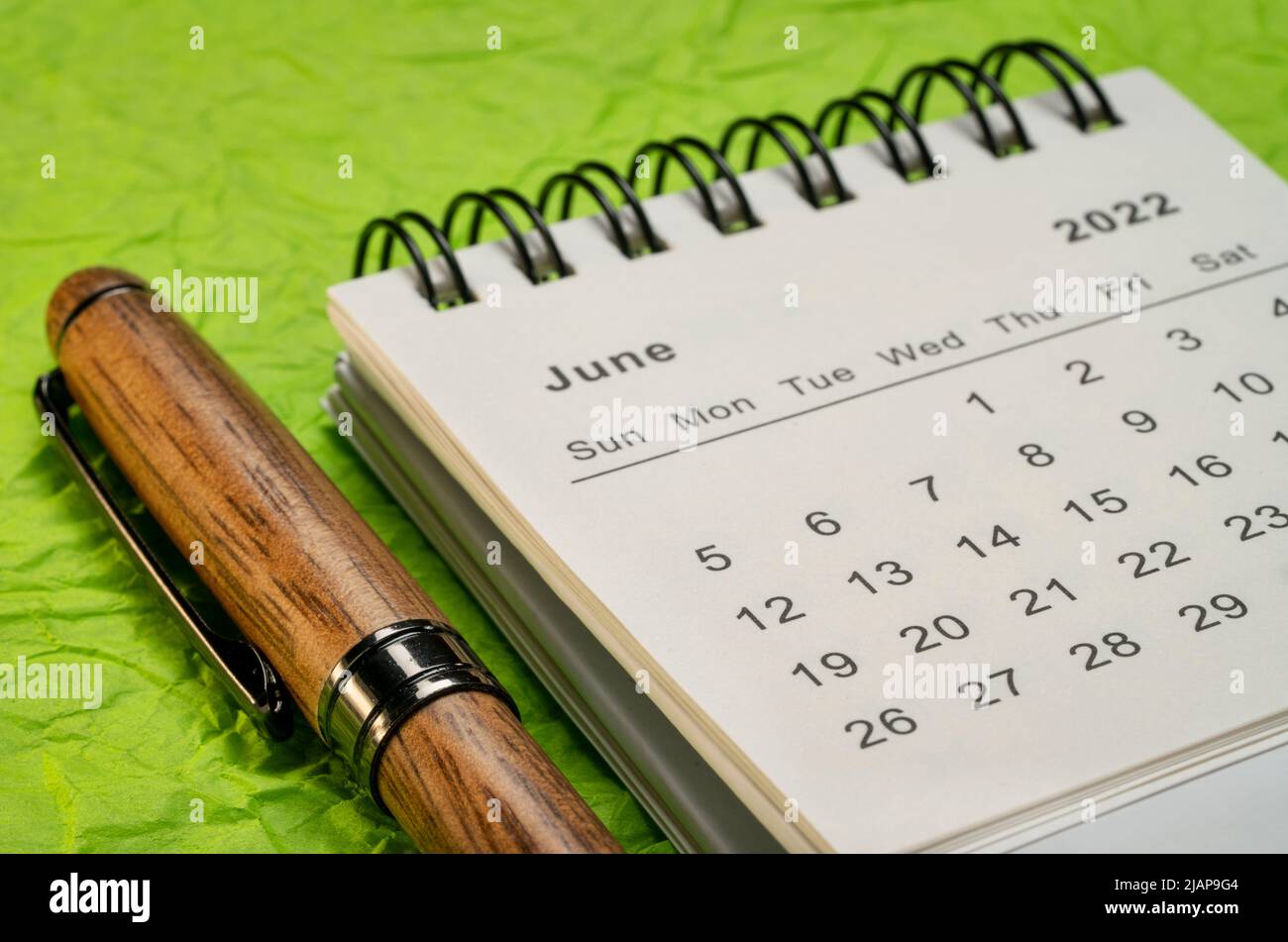 Juni 2022 - Spiralkalender mit Stift gegen knallgrünes handgemachtes Papier, Zeit- und Geschäftskonzept Stockfoto