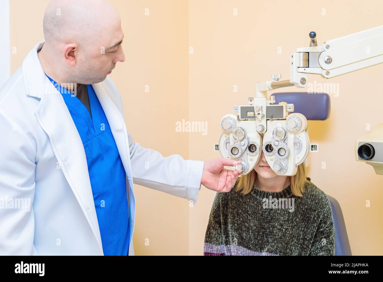 Ein männlicher Augenarzt überprüft das Augenlicht eines Mädchens mit einem Phoropter. Sehbehandlung. Stockfoto