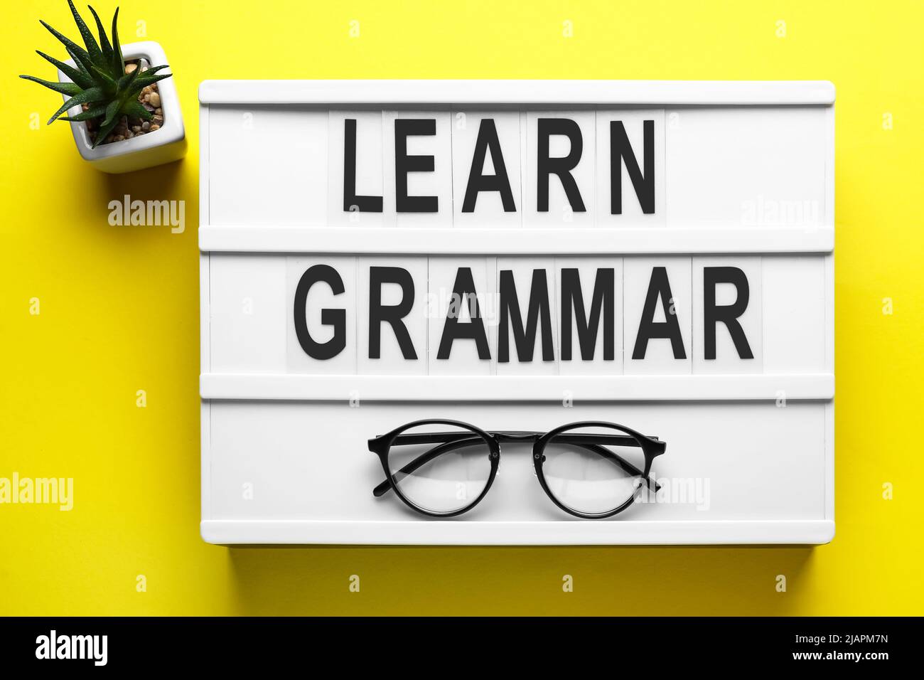 Brett mit Text GRAMMATIK LERNEN, Brillen und Blumentopf auf gelbem Hintergrund Stockfoto