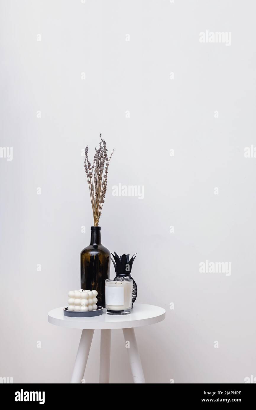 Vase und Kerzen auf einem kleinen Tisch über der weißen Wand, minimalistisches Wohndekor Stockfoto