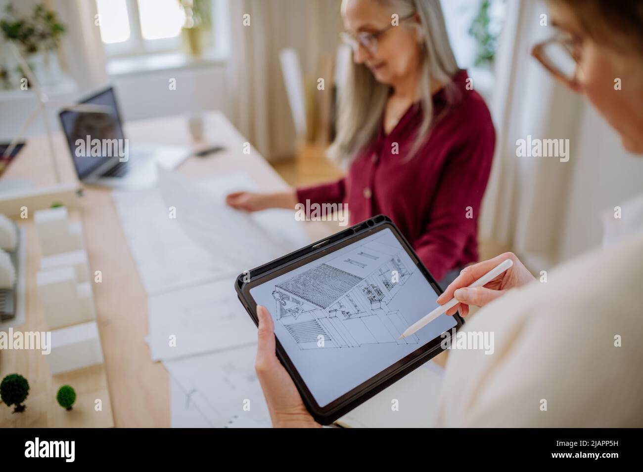 Reife Frauen arbeiten als Öko-Architektinnen mit Blaupausen gemeinsam im Büro an Tablets. Stockfoto