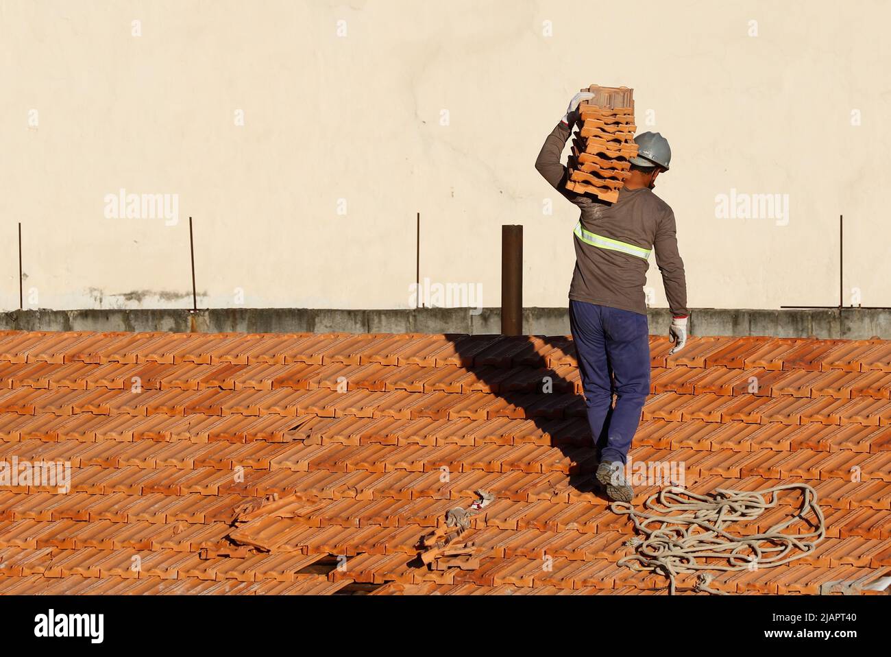 Mann arbeitet an der Dachinstallation. Dachkonstruktion. Reparatur des Ziegeldachs. Haus im Bau. Arbeiter renoviert Abdichtung Dach des Gebäudes. Stockfoto