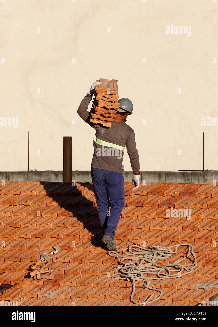 Mann arbeitet an der Dachinstallation. Dachkonstruktion. Reparatur des Ziegeldachs. Haus im Bau. Arbeiter renoviert Abdichtung Dach des Gebäudes. Stockfoto