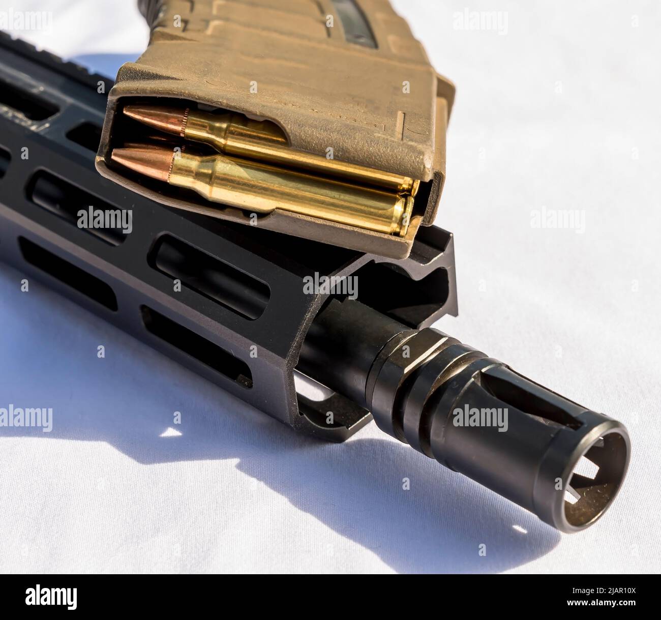Die Mündung und der Lauf eines AR 15-Gewehr unter einem Gewehrmagazin, das mit Kugeln des Kalibers 223 auf weißem Grund beladen ist Stockfoto