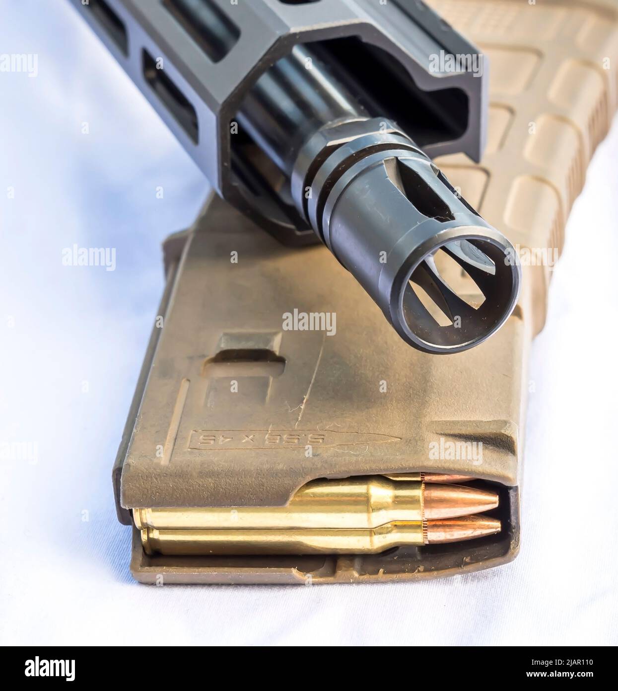 Die Mündung und der Lauf eines AR 15-Gewebes auf einem Gewehr-Magazin, das mit Kugeln des Kalibers 223 auf weißem Grund beladen ist Stockfoto