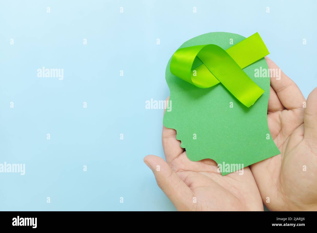 Hand hält das menschliche Kopfprofil mit einem hellgrünen Bewusstseinsband am Gehirn. Lyme-Borreliose, Psychose, psychische Erkrankungen im Kindesalter, Lymphom und postpartum Stockfoto